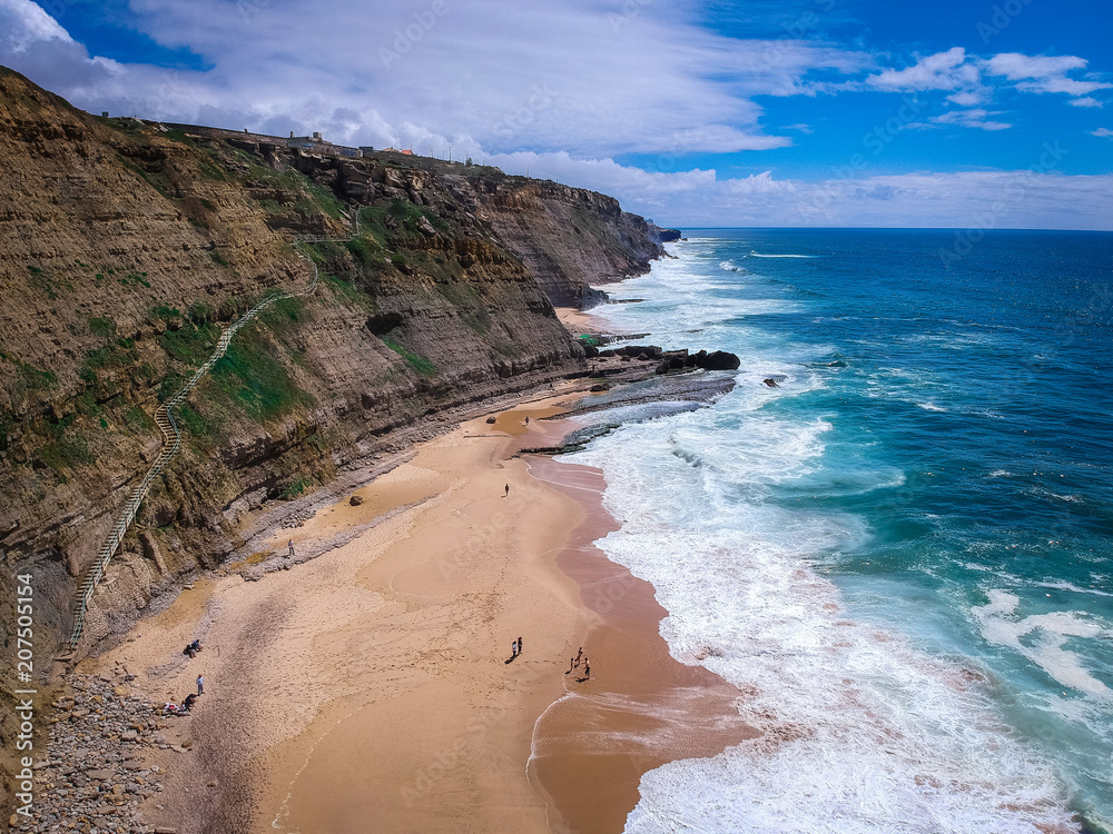 Aerial view of  a cliff in the portuguese coastline. Sand beach aerial, top view of a beautiful sandy beach aerial shot with the blue waves rolling into the shore