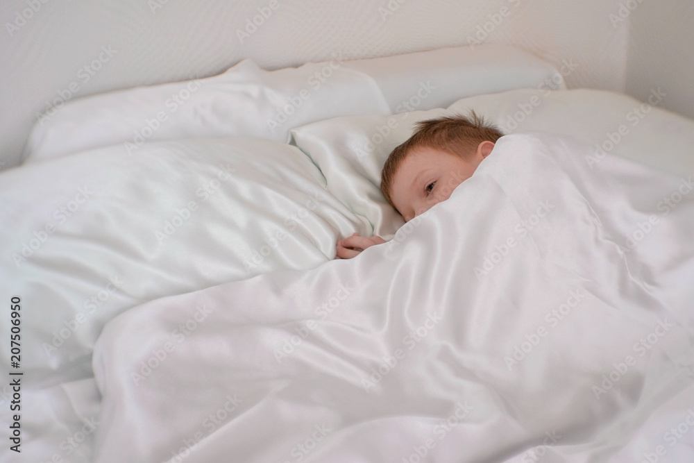Seven-year-old boy wakes up in his bed under the blanket Seven-year-old boy wakes up in his bed under the blanket
