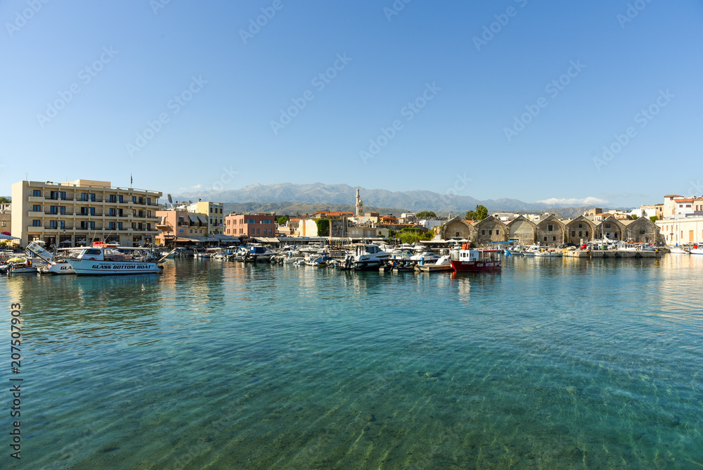 View of the Venetian port of Chania with the ancient venetian shipyards and the pleasure boats. In the back, the white mountains