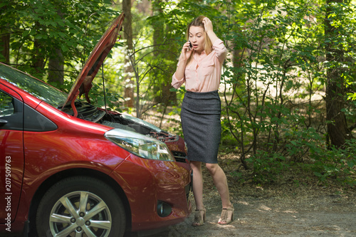 A girl with a broken car that smokes, with a phone, calls for help in a service, or an insurance