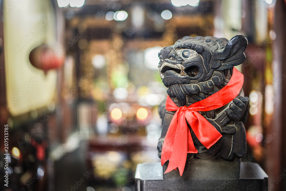 Smart black stone lion statue glance at the right side, red scarf and blur background Smart black stone lion statue glance at the right side, red scarf and blur background
