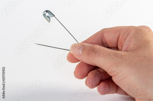 Single opened metal safety pin in the hand of a woman isolated on white background
