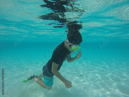 Child boy swimming diving snorkelling in a clear water on sandy beach looking for coral fish in new caledonia