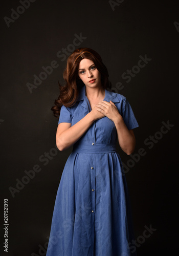 3/4 portrait of brunette lady wearing blue dress. posed on black studio background.
