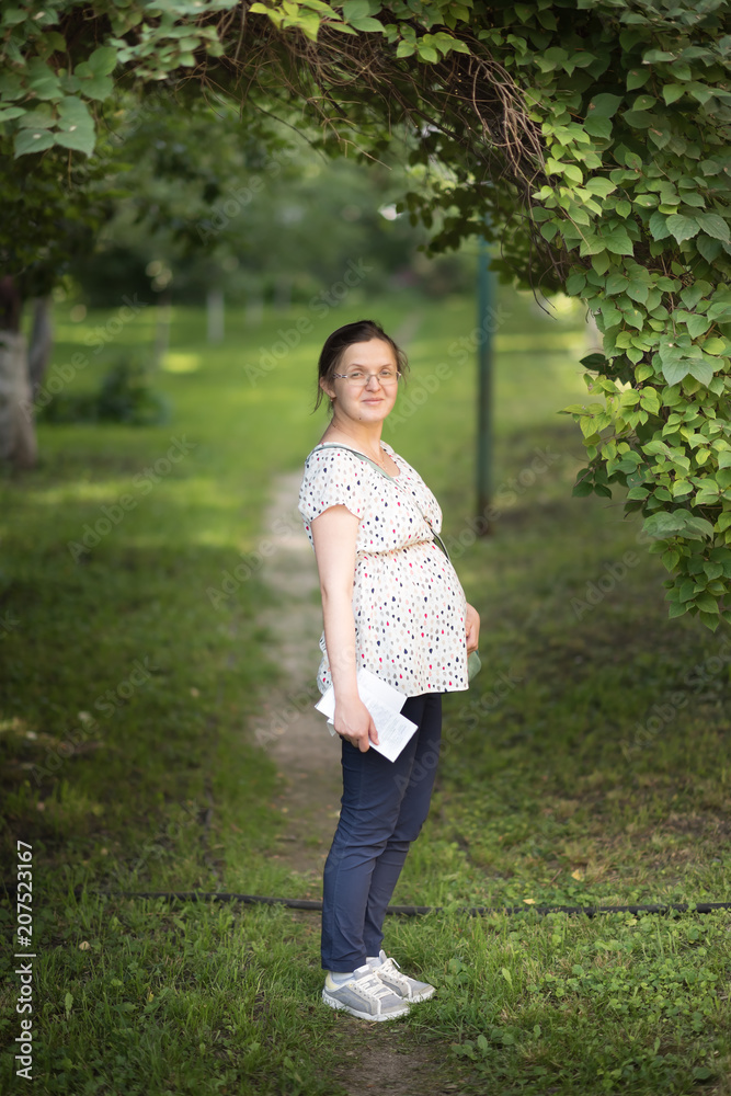 Attractive pregnant girl is standing under the tree in summer park Attractive pregnant girl is standing under the tree in summer park