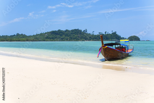 Wooden boat on a white sand beach, blue sea with islands in background, tropical beach in Thailand
