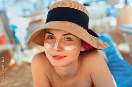 Woman smile applying sun cream  on face. Skincare. Body Sun protection. sunscreen. Female in hat smear  moisturizing lotion on skin.