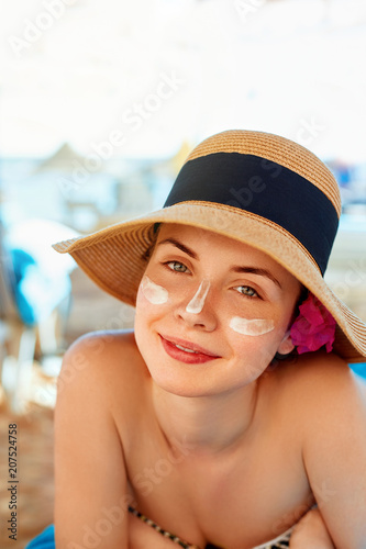Facial Care. Female Applying Sun Cream and Smiling. Beauty Face.  Portrait Of Young Woman in hat Smear  Moisturizing Lotion on Skin. SkinCare