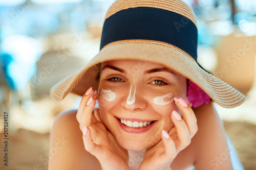 Skincare. Beauty Concept. Young pretty woman applying sun cream  and touch own face. Female in hat smear  sunscreen lotion on skin. Skin Protection and dermatology.