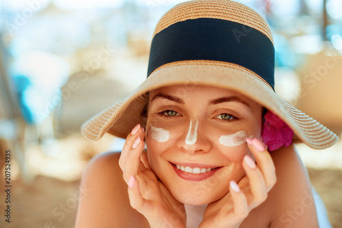 .Woman smile applying sun cream  on face. Skincare. Body Sun protection. sunscreen. Female in hat smear  moisturizing lotion on skin.