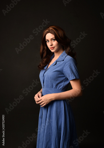 3/4 portrait of brunette lady wearing blue dress. posed on black studio background.
