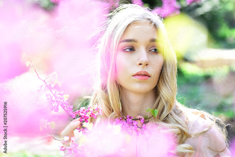 Fototapeta premium Spring bloom concept. Young woman enjoy flowers in garden, defocused, close up. Girl on dreamy face, tender blonde near violet flowers of judas tree, nature background. Lady in park on spring day.