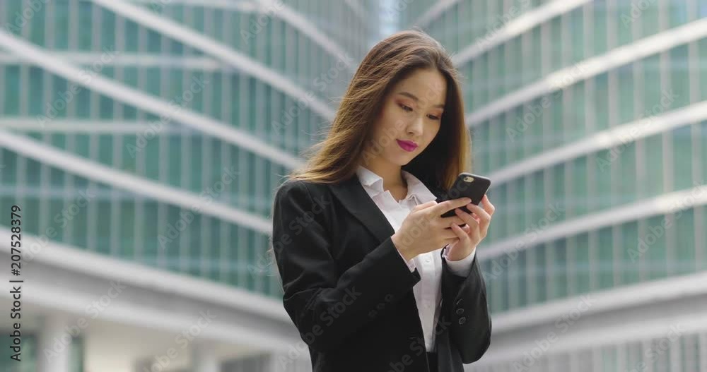 An asian business woman, she is happy and smiling while sending messages, working emails or calling using the phone, outside the office. Concept of: technology, network, oriental An asian business woman, she is happy and smiling while sending messages, working emails or calling using the phone, outside the office. Concept of: technology, network, oriental