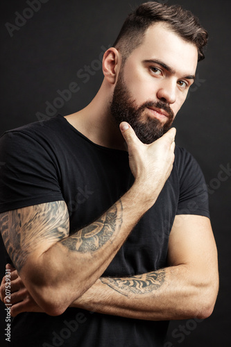 Portrait of confident bearded man bodybuilder dressed in tight black t-shirt standing over black background. photo