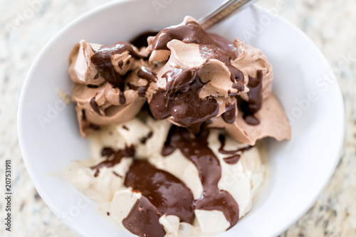 Soft serve vanilla and chocolate ice cream with dark brown syrup drizzled sauce closeup in white bowl with spoon