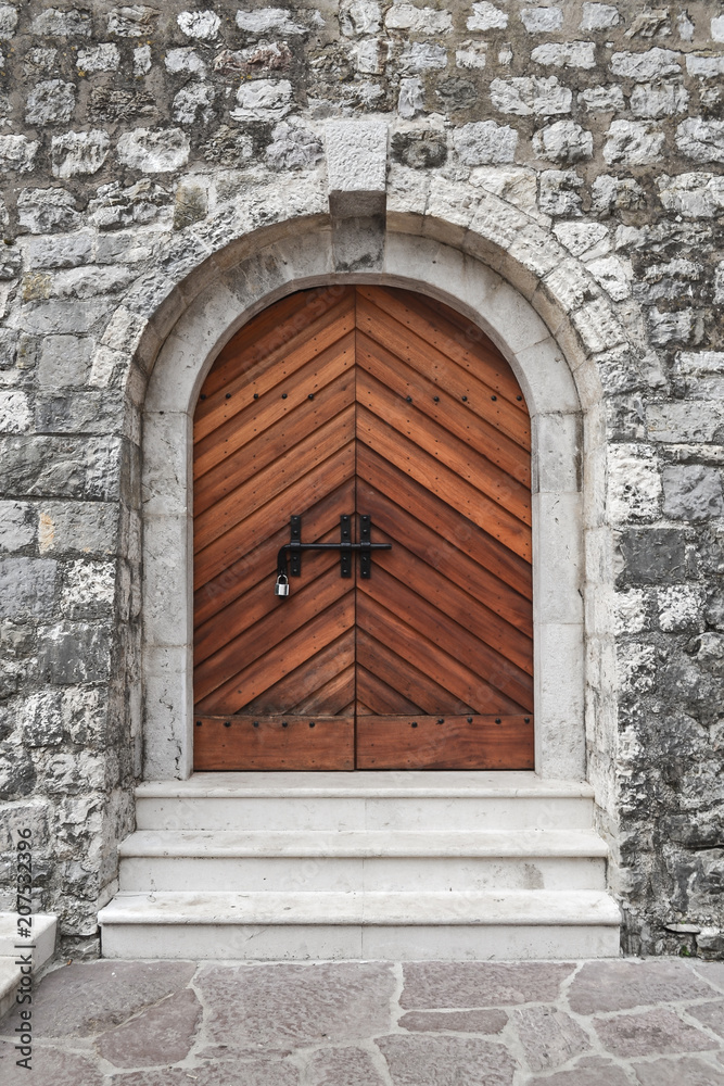 The stone fortress wall of the castle of the medieval castle, an old wooden closed door with a lock.