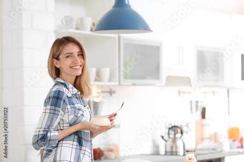 Young attractive woman eating tasty yogurt in kitchen