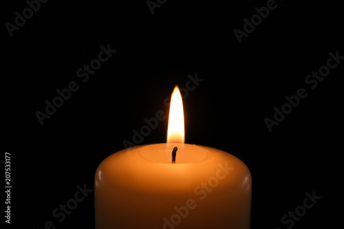 Wax candle burning on black background, closeup