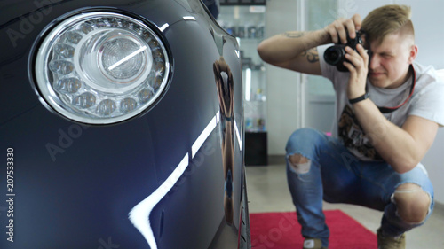 A young professional photographer (a guy, a man) takes pictures of a car in a car salon. Concept: lifestyle, new photo, car, photo apron, flash, exhibition. photo