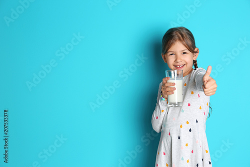Cute little girl with glass of milk on color background
