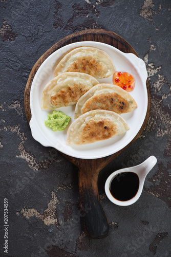 White plate with fried potstickers on a rustic wooden serving board, vertical shot on a brown stone background, top view