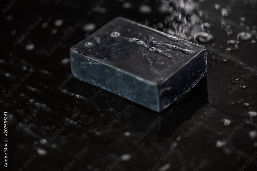 block of natural carbon charcoal soap on black stone background with bubbles block of natural carbon charcoal soap on black stone background with bubbles