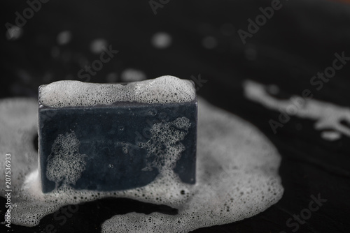 block of natural carbon charcoal soap on black stone background with bubbles