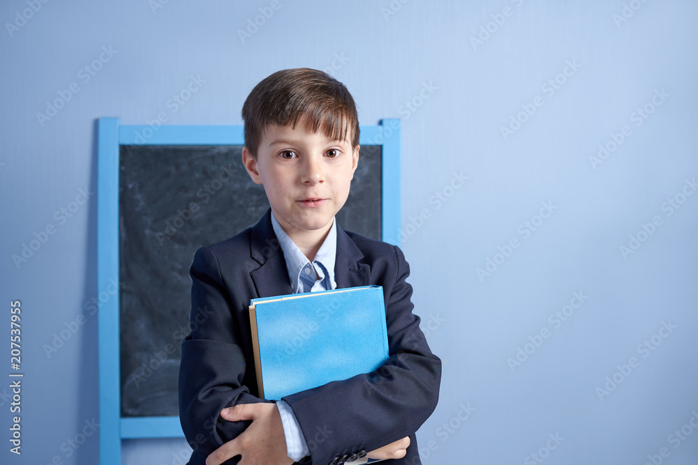Cheerful European schoolboy with book in uniform in a classroom. First time to school. Back to school. Cheerful European schoolboy with book in uniform in a classroom. First time to school. Back to school.