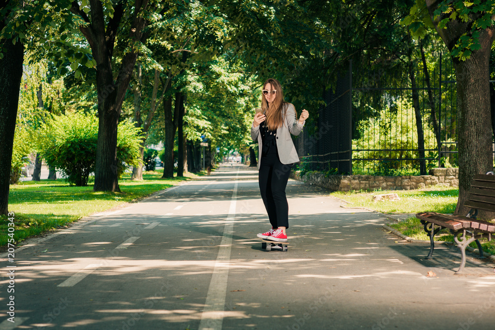 Fototapeta premium Young business woman riding a skateboard in the park