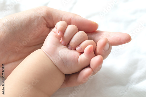 Mother uses her hand to hold her baby's tiny hand to make him feeling her love, warm, comfort and secure.