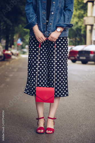 stylish woman in polka dot culottes and red high heel shoes holding a red purse and crossing the road. street style fashion