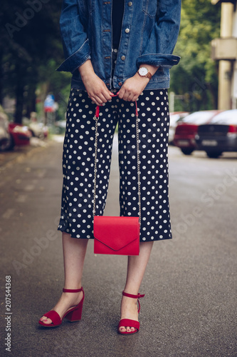 stylish woman in polka dot culottes and red high heel shoes holding a red purse and crossing the road. street style fashion