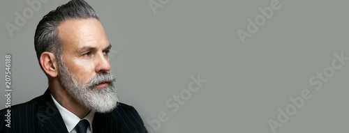 Close-up portrait of bearded gentleman wearing trendy suit over empty gray background. Copy Paste text space. Wide.