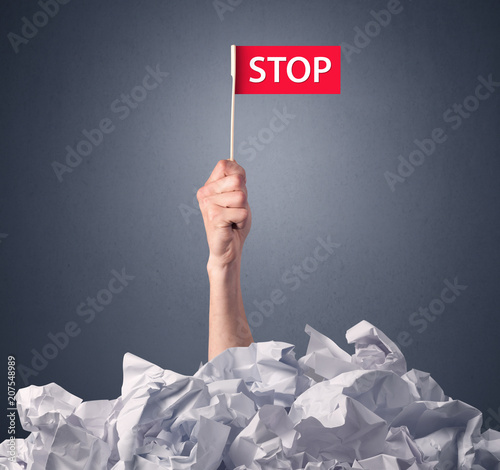 Cuadro en lienzo Female hand emerging from crumpled paper pile holding a red flag with stop writt
