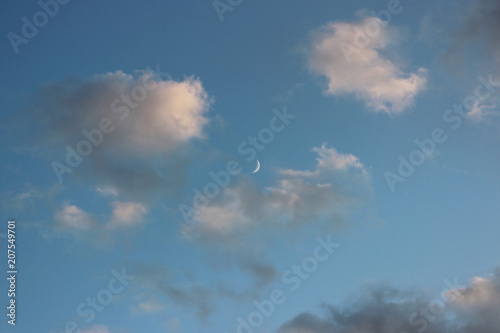 a thin crescent in the early evening is visible in the sky among the white clouds