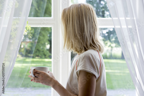 Young girl enjoying her morning coffee or tea, looking out the window.