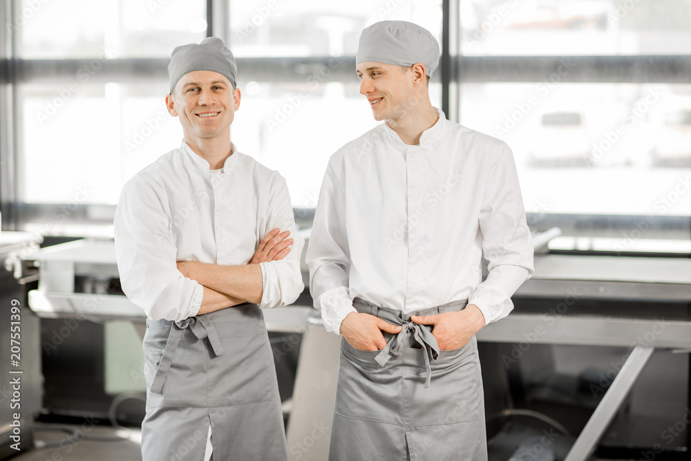 Portrait of a two handsome bakers in uniform standing indoors at the modern bakery manufacturing