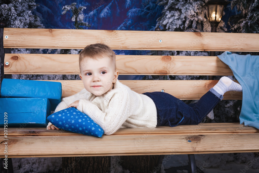small baby boy laying on the wooden bench holding a blue pillow with snowflakes indoor small baby boy laying on the wooden bench holding a blue pillow with snowflakes indoor