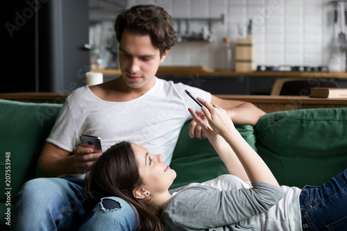 Millennial couple obsessed with smartphones checking social networks at home using phone apps relaxing together on sofa lost in news online, young man and woman texting or browsing on cellphones © fizkes