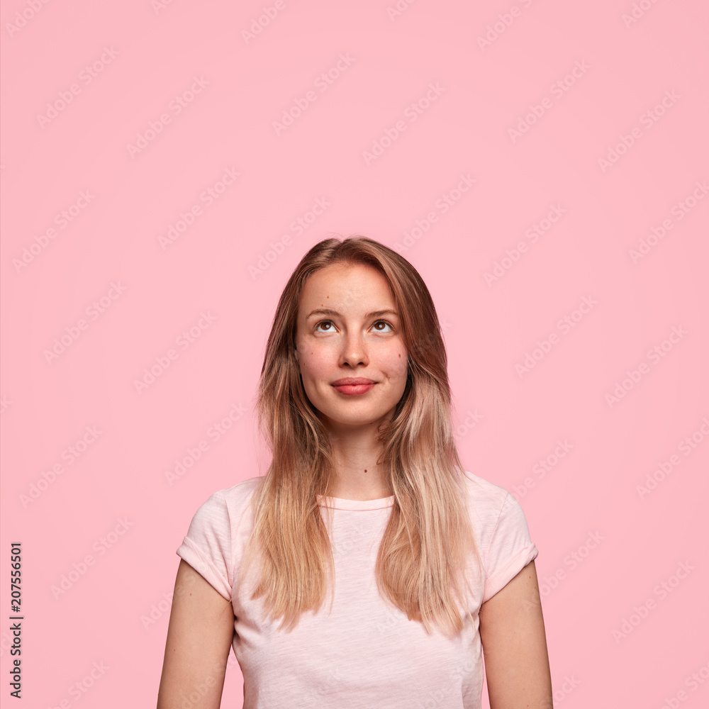 Beautiful Caucasian female looks happily upwards, sees something appealing, rejoices buying new chandelier, wears casual clothing, isolated over pink background with blank copy space for promotion Beautiful Caucasian female looks happily upwards, sees something appealing, rejoices buying new chandelier, wears casual clothing, isolated over pink background with blank copy space for promotion