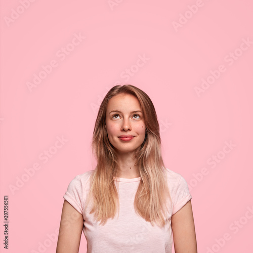 Beautiful Caucasian female looks happily upwards, sees something appealing, r...