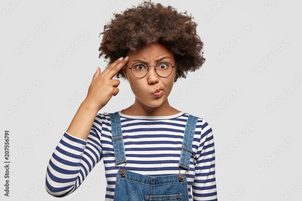 Displeased dark skinned female being tired of everything, makes suicide gesture and imitates gun with hand, curves lips, keeps two fingers on temple, shoots. African American woman gestures indoor Displeased dark skinned female being tired of everything, makes suicide gesture and imitates gun with hand, curves lips, keeps two fingers on temple, shoots. African American woman gestures indoor