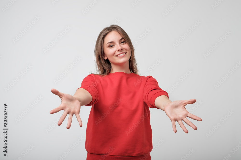 portrait of attractive smile teenage girl raised up arms hands at you. She is dressed in red t-shirt. Happy to welcome a friend or guest - obrazy, fototapety, plakaty 