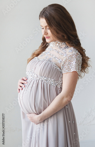 A pregnant woman with long hair and in a beautiful long dress. Pregnant hugs belly