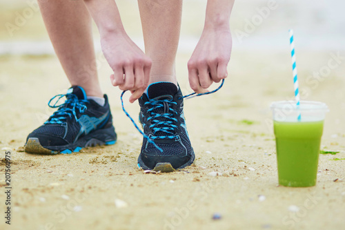 Jogger with green vegetable smoothie  tying sport running shoes laces