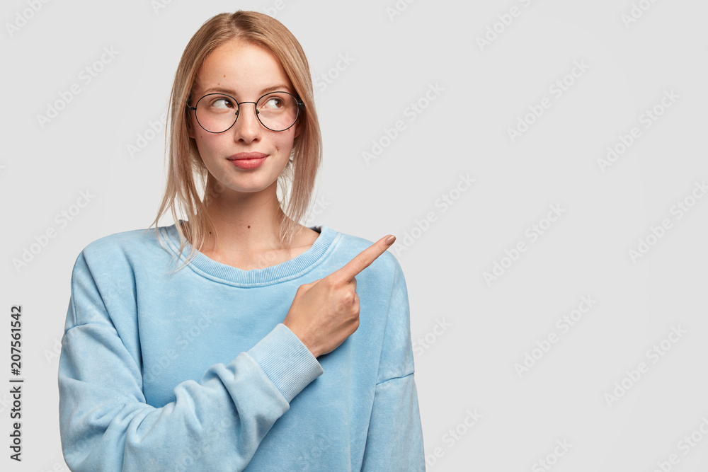 Attractive Caucasian female with slightly combed hair, wears casual oversized sweater, indicates with fore finger at right upper corner, shows blank space for your advertisement or promotion Attractive Caucasian female with slightly combed hair, wears casual oversized sweater, indicates with fore finger at right upper corner, shows blank space for your advertisement or promotion