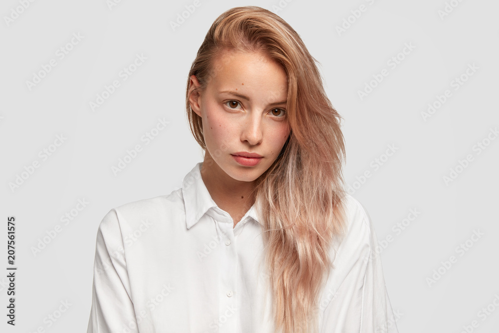 Close up portrait of lovely European female with pure skin and straight hair, looks at camera with appeal, wears casual white shirt, poses indoor, has facial treatment. Beauty and health concept Close up portrait of lovely European female with pure skin and straight hair, looks at camera with appeal, wears casual white shirt, poses indoor, has facial treatment. Beauty and health concept