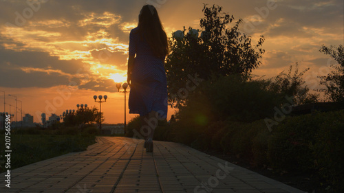 Girl walking away through park at the sunset. Slide.