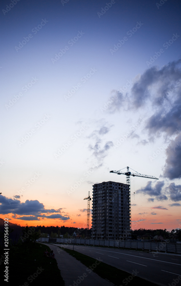 Crane and construction site against sunset. Unfinished building construction and building cranes against blue sky background. Concept of urban development