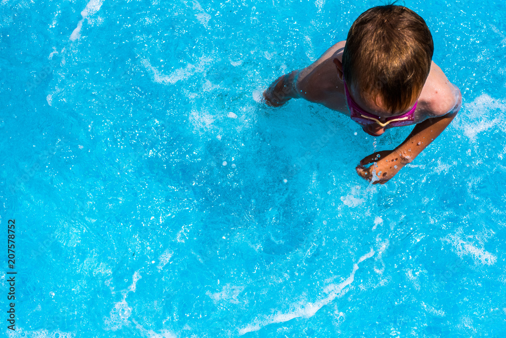 Child splashing in the cool water of a pool in summer